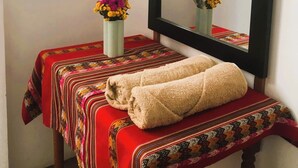 A bathroom with a large mirror, a bench with towels, and two vases with flowers.
