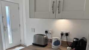 Une cuisine moderne avec des meubles blancs, un plan de travail en bois, un grille-pain, une bouilloire et une machine à café.
