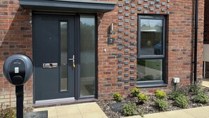 Un bâtiment moderne en briques, doté d’une porte d’entrée de couleur sombre, d’une petite fenêtre et d’un parcmètre installé sur le trottoir.