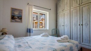 Un dormitorio con cama, ventana con cortinas, una silla y un armario.