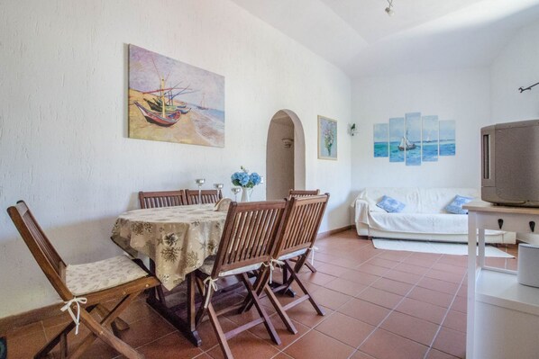 A dining area with a table set for four, a white sofa, and a television in the living room.