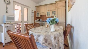 Un comedor con una mesa preparada para cuatro personas, un televisor sobre un mueble bajo y una cocina al fondo.