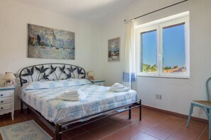 A bedroom with a bed, two bedside tables, a window with a view, and artwork on the wall.