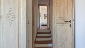 Un pasillo con puertas de madera, una escalera y una cama al fondo.
