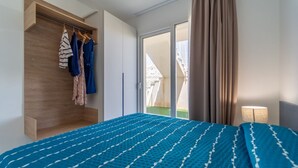 Une chambre d’hôtel avec un lit, une armoire en bois, un portant à vêtements et une vue sur l’extérieur, visible à travers une porte vitrée.
