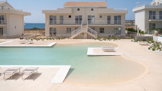 Un hôtel moderne doté d’une piscine, de chaises longues et offrant une vue sur la mer.