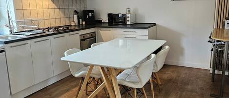 Eine moderne Küche mit weißen Schränken, Holzboden und einem Essbereich mit weißem Tisch und Stühlen.