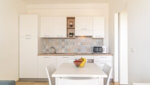 Een moderne keuken met witte kastjes, een betegelde achterwand, een magnetron en een eettafel met stoelen.
