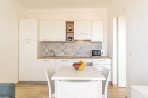 A modern kitchen with white cabinets, a tiled backsplash, a microwave, and a dining table with chairs.