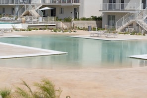 Une piscine avec des chaises longues, un escalier et un bâtiment doté de balcons.