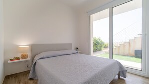 A bedroom with a bed, a nightstand, a lamp, and a window with a view of the outdoors.