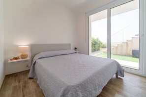 A bedroom with a bed, a nightstand, a lamp, and a window with a view of the outdoors.