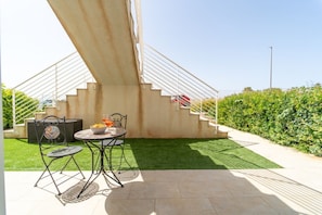 A patio with a table and chairs, a staircase, and a green lawn.