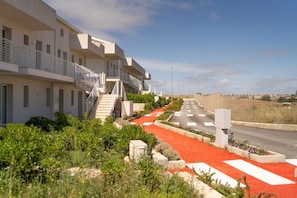 A modern building with multiple balconies, a red carpeted pathway, and a clear sky.