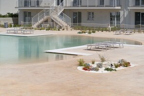 A swimming pool with lounge chairs, a staircase, and a building with a balcony.