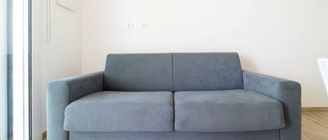 Un sofá gris en una habitación con suelo de madera y pared blanca.