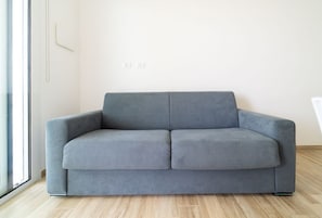 A grey sofa in a room with a wooden floor and a white wall.