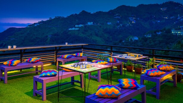 A rooftop terrace with multiple tables and benches, some with colorful cushions. - goSTOPS Mussoorie Library Road (Mussoorie)