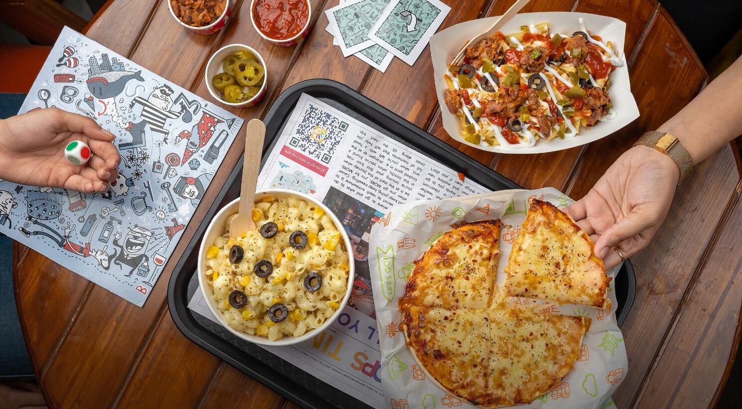 A dining table with a pizza, a bowl of pasta, and a tray of nachos.