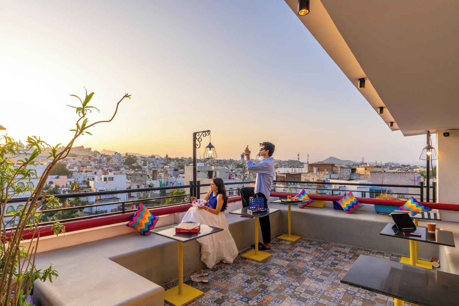 A rooftop terrace with a city view, a table with a laptop, and a person taking a photo.