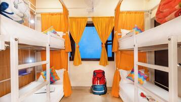 A dormitory room with bunk beds, orange curtains, a fan, and a red backpack on the floor.
