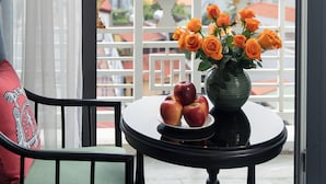 Un balcon avec une table sur laquelle se trouve un vase rempli de fleurs et des pommes, une chaise, et une vue sur les bâtiments.