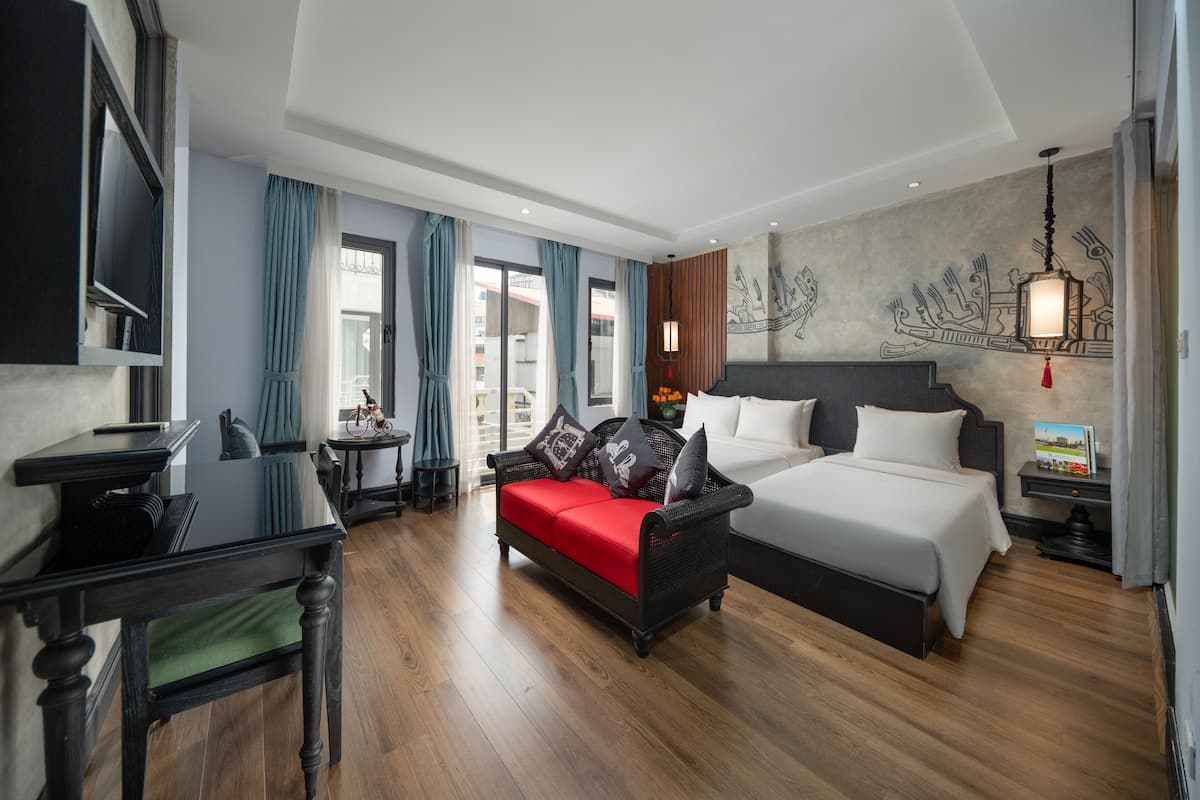 A modern hotel room with a large bed, a sofa, a desk, and a TV.