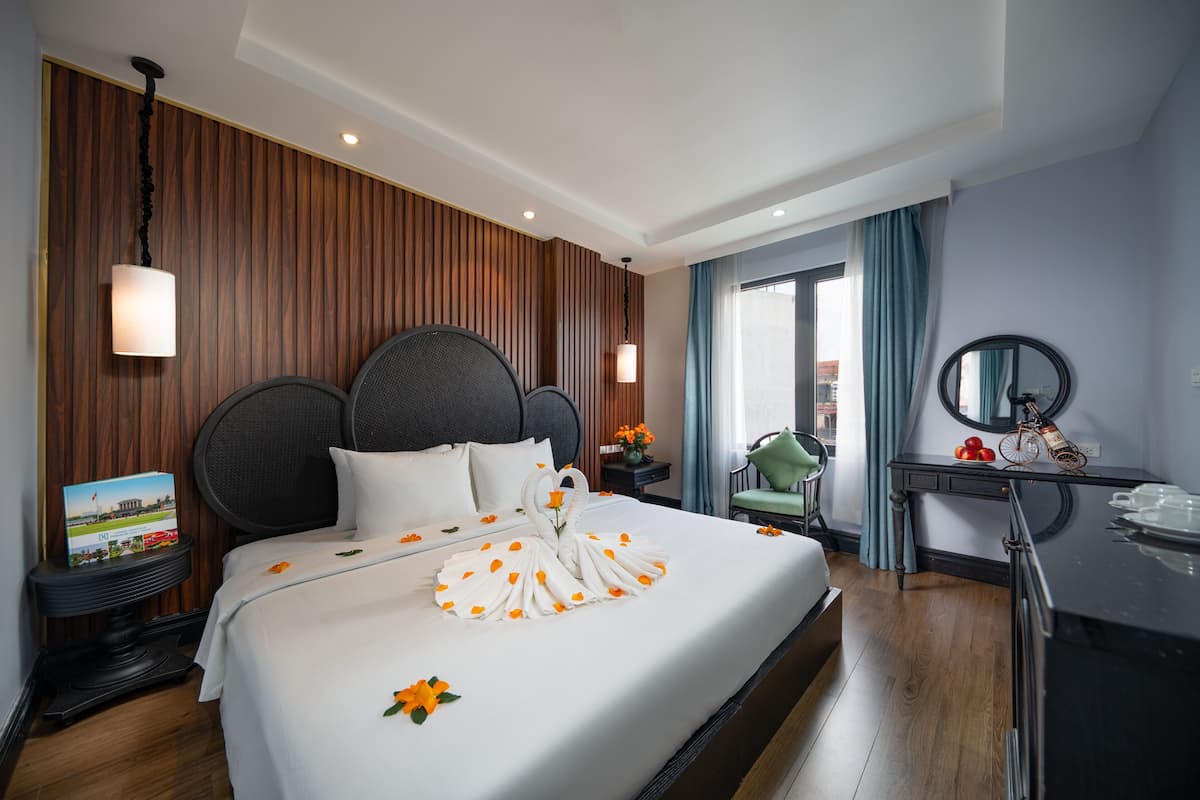 A hotel room with a large bed, wooden paneling, a desk with a mirror, and a view of the city through the window.