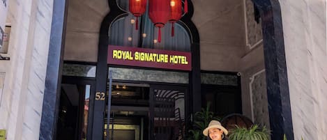 The entrance of the Royal Signature Hotel with a sign above the door, a staircase leading up, and a person with a suitcase.
