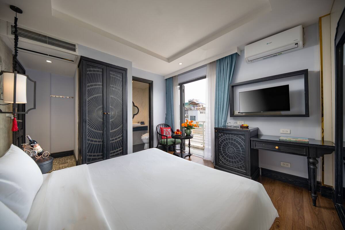 A hotel room with a bed, a desk, a TV, and a view of the outside.