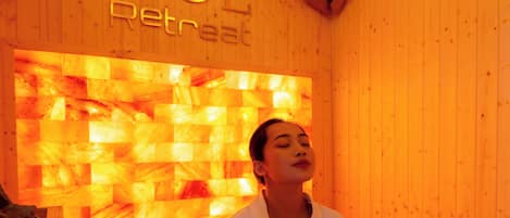 A person seated on a floor covered with pebbles in a wooden room with a wall displaying the text "SOL Retreat".