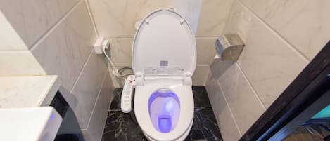 Un baño moderno con inodoro, control remoto y piso de mármol.