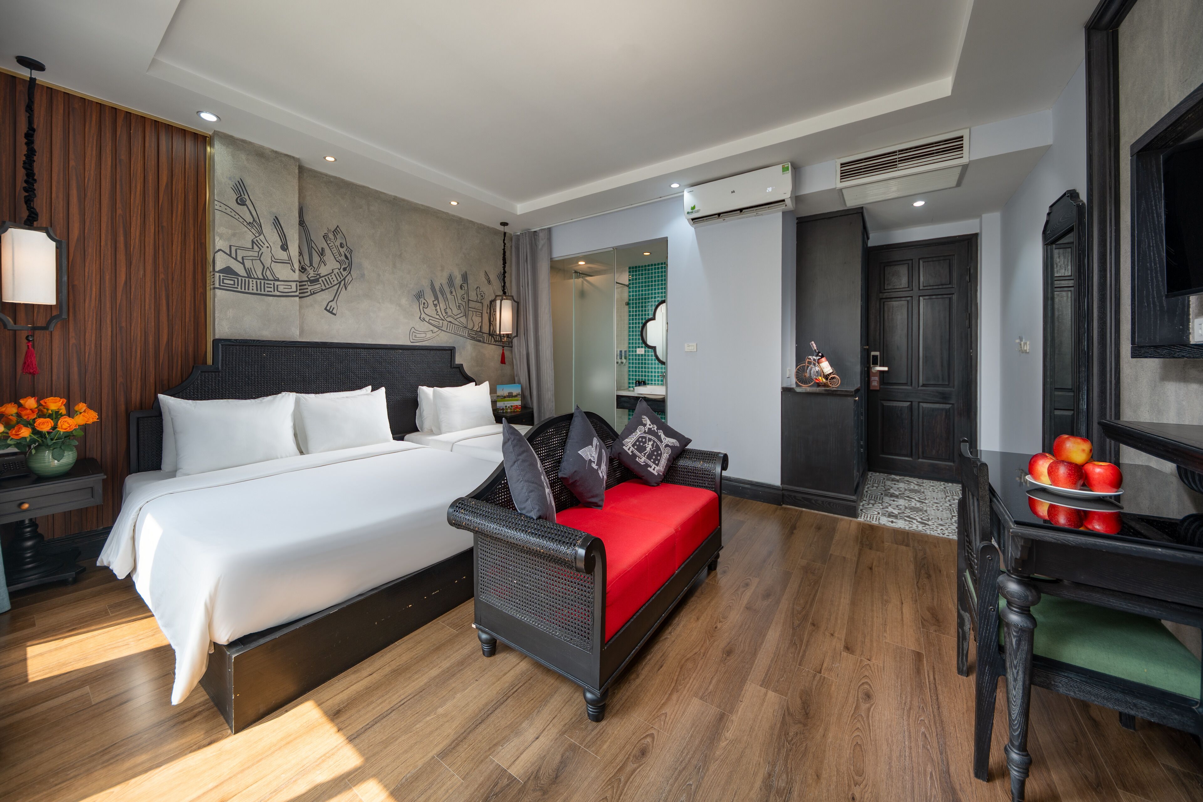 A modern hotel room with a large bed, a sofa, and a desk with apples.