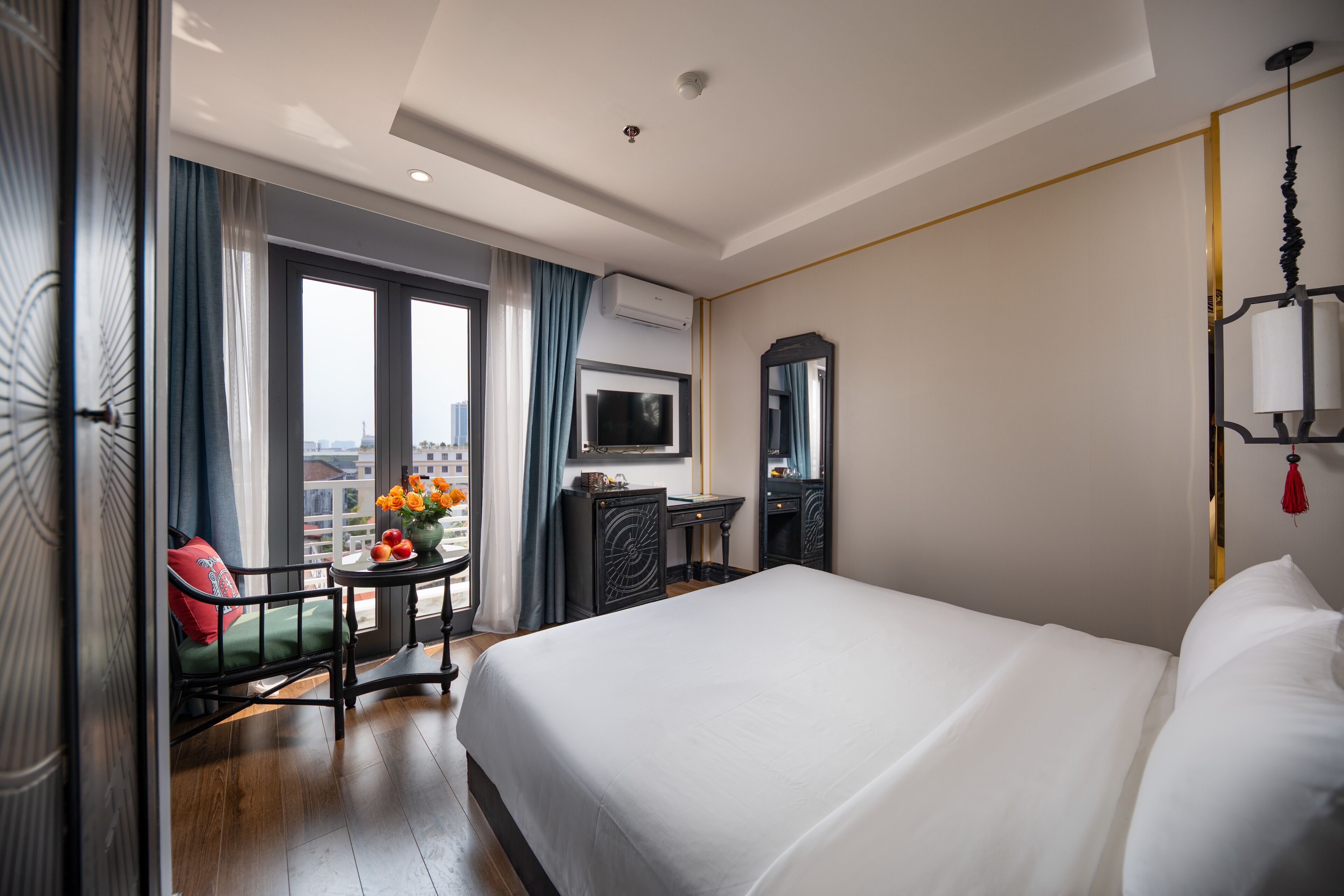 A hotel room with a large bed, a desk with a chair, a TV, and a view of the city through the window.