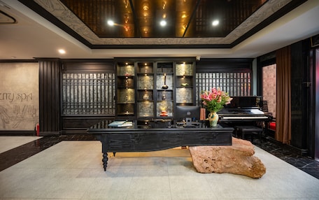 A reception area with a black reception desk, a piano, and a decorative wall with shelves.
