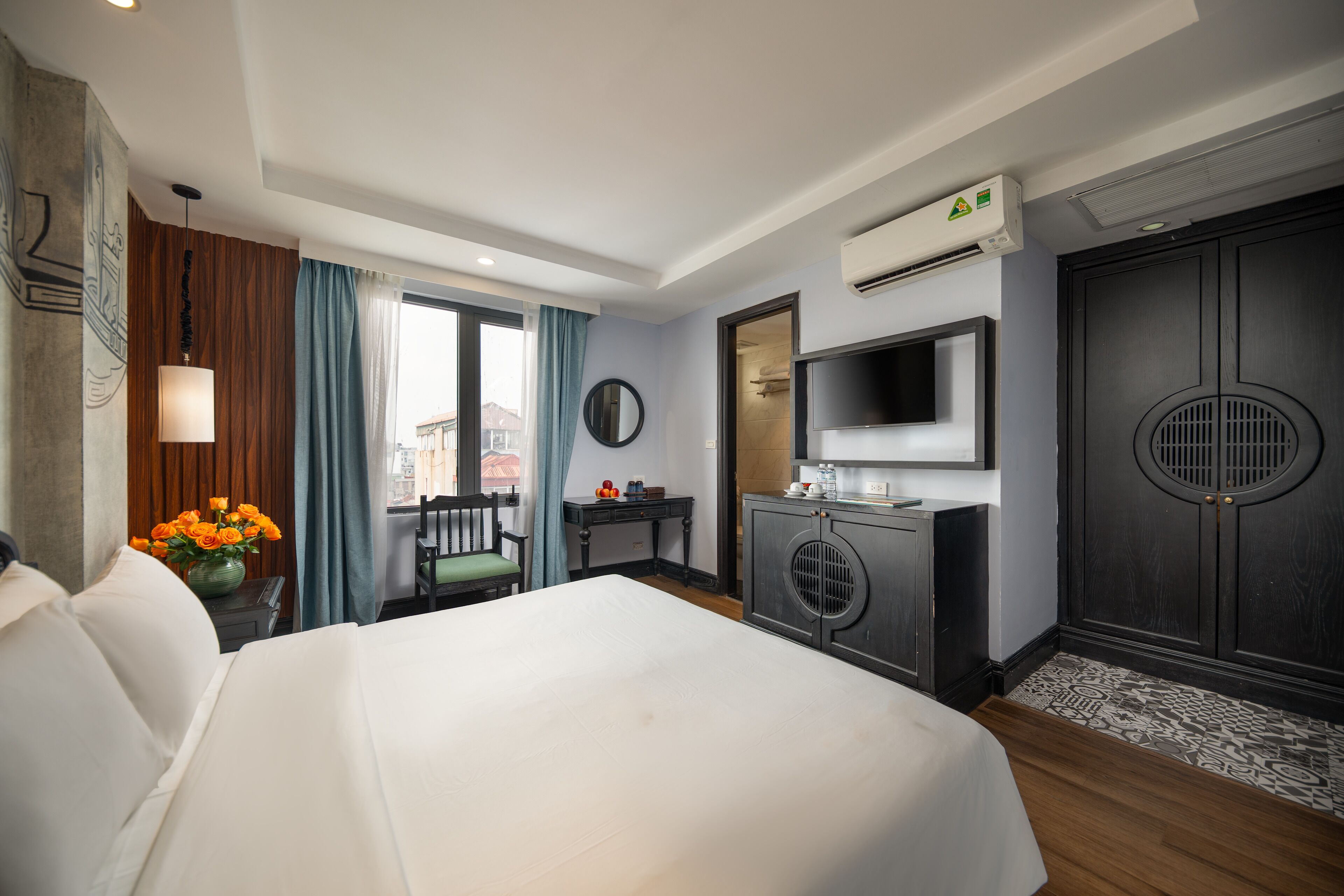 A hotel room with a bed, a desk, a TV, and an air conditioning unit.