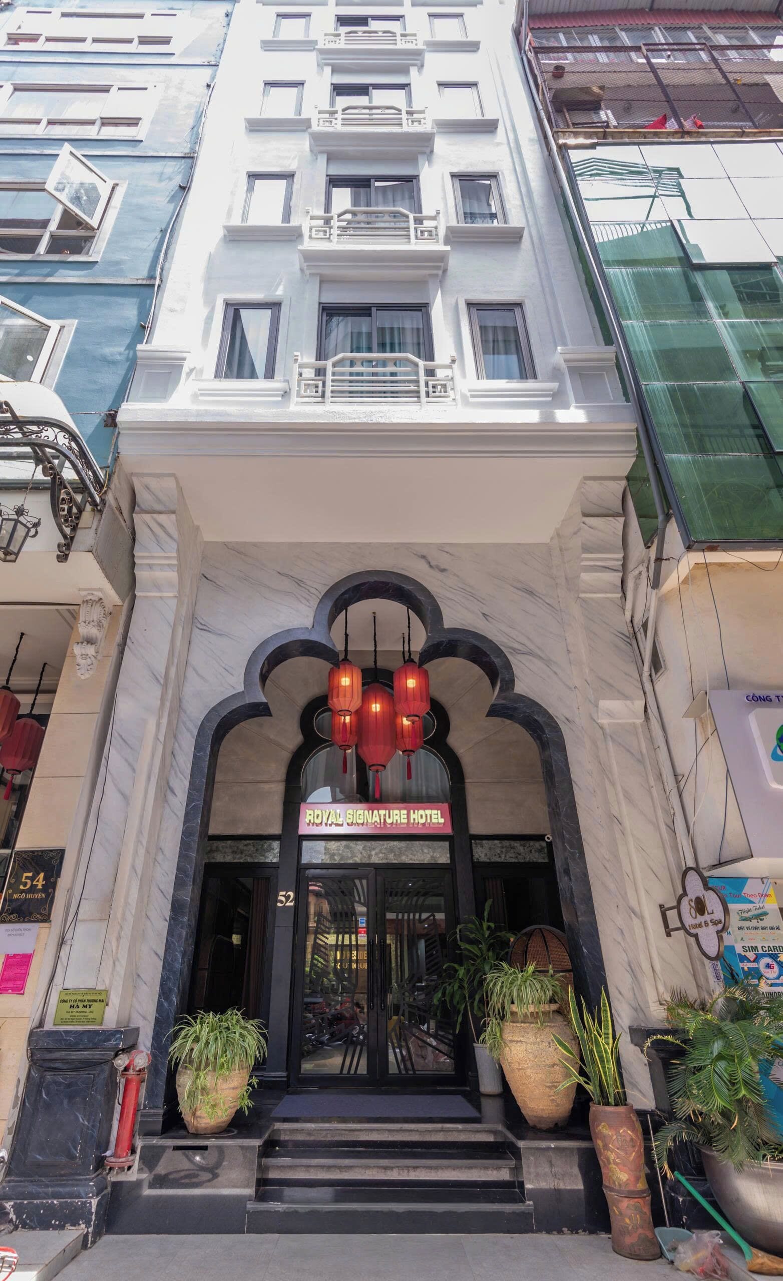 The entrance of the Royal Signature Hotel with a marble facade, a signboard, and traditional red lanterns.