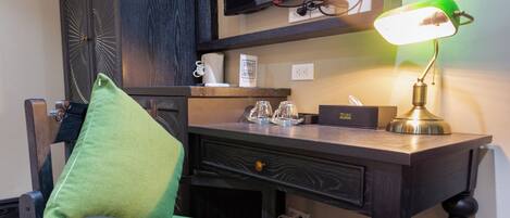 Un escritorio de madera con un televisor, una lámpara y una silla con un cojín verde.