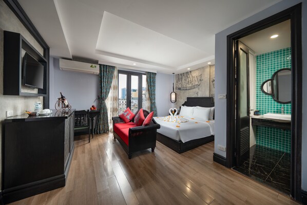 A hotel room with a bed, a sofa, a TV, and a bathroom with a mirror and sink. -  Royal Signature Hotel Hanoi (Hanoi)