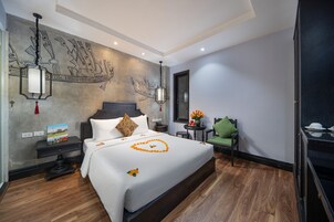 A hotel room with a large bed, a wall mural, a small table with flowers, and a green chair.