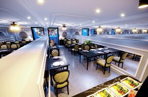 A spacious restaurant with multiple dining tables and chairs, a buffet area with various food options, and a modern ceiling design with recessed lighting.