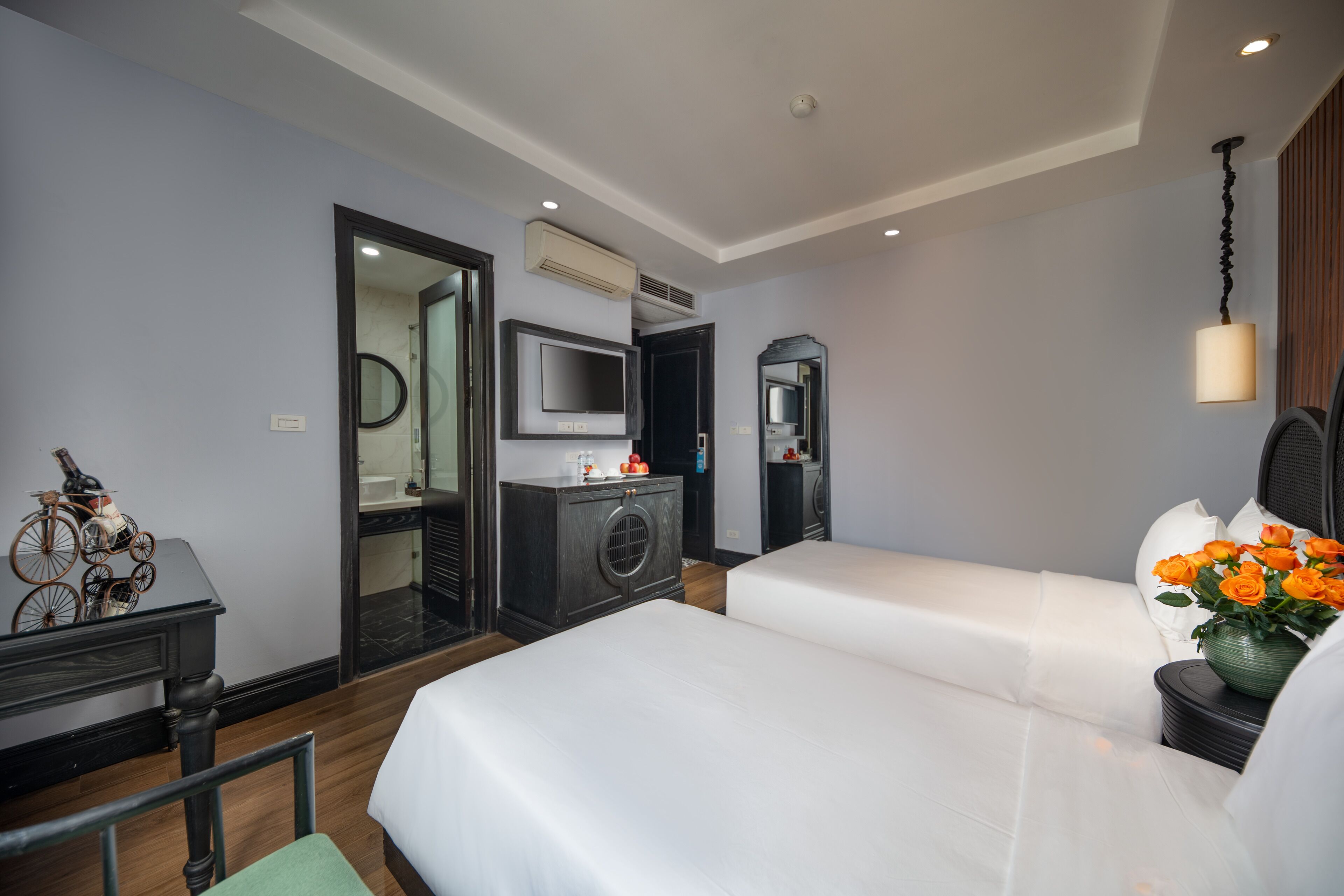Ein Hotelzimmer mit zwei Betten, einem Fernseher, einem Spiegel, einer Kommode und einem kleinen Tisch mit einer Blumenvase.