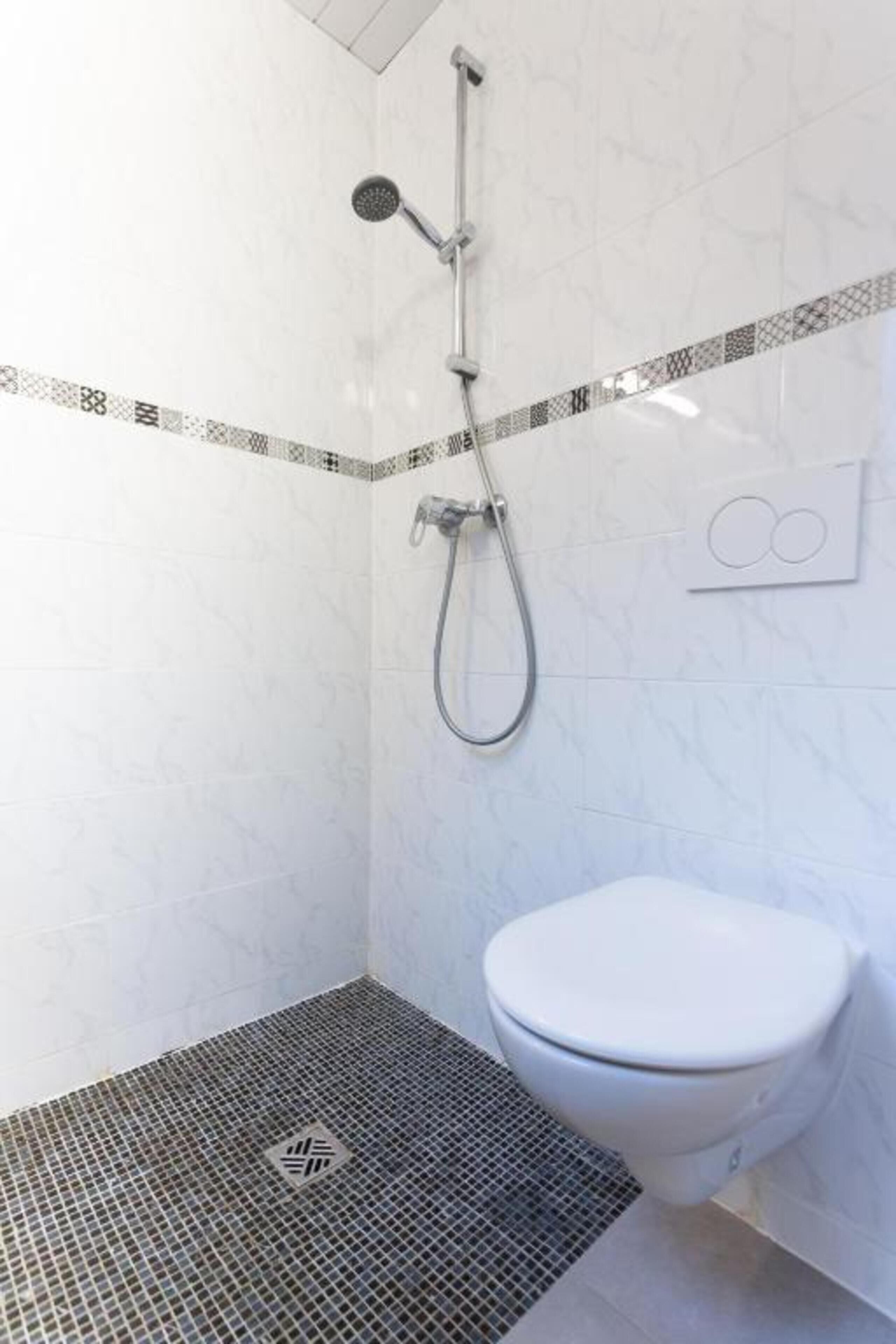 Ein Badezimmer mit Dusche, Toilette und Fliesenboden.