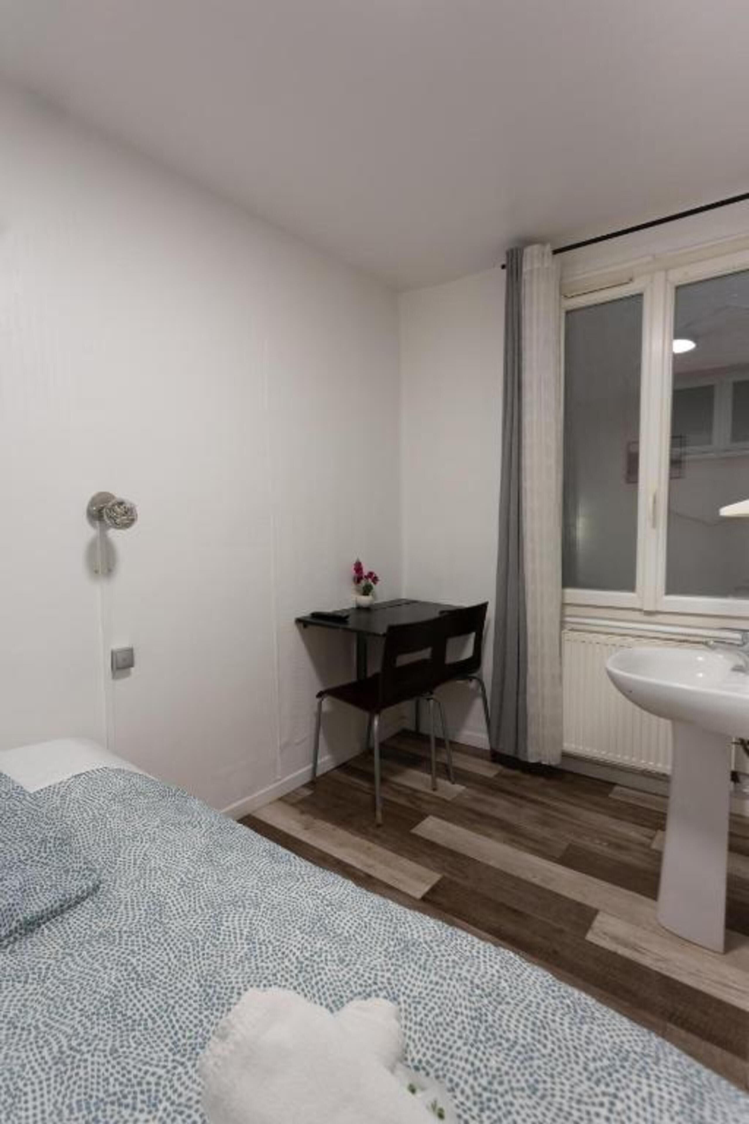 A small, clean room with a bed, a desk, and a window.