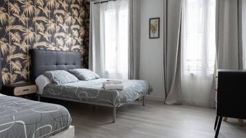 A modern bedroom with two beds, a large window with sheer curtains, and a wall with a tropical leaf pattern.