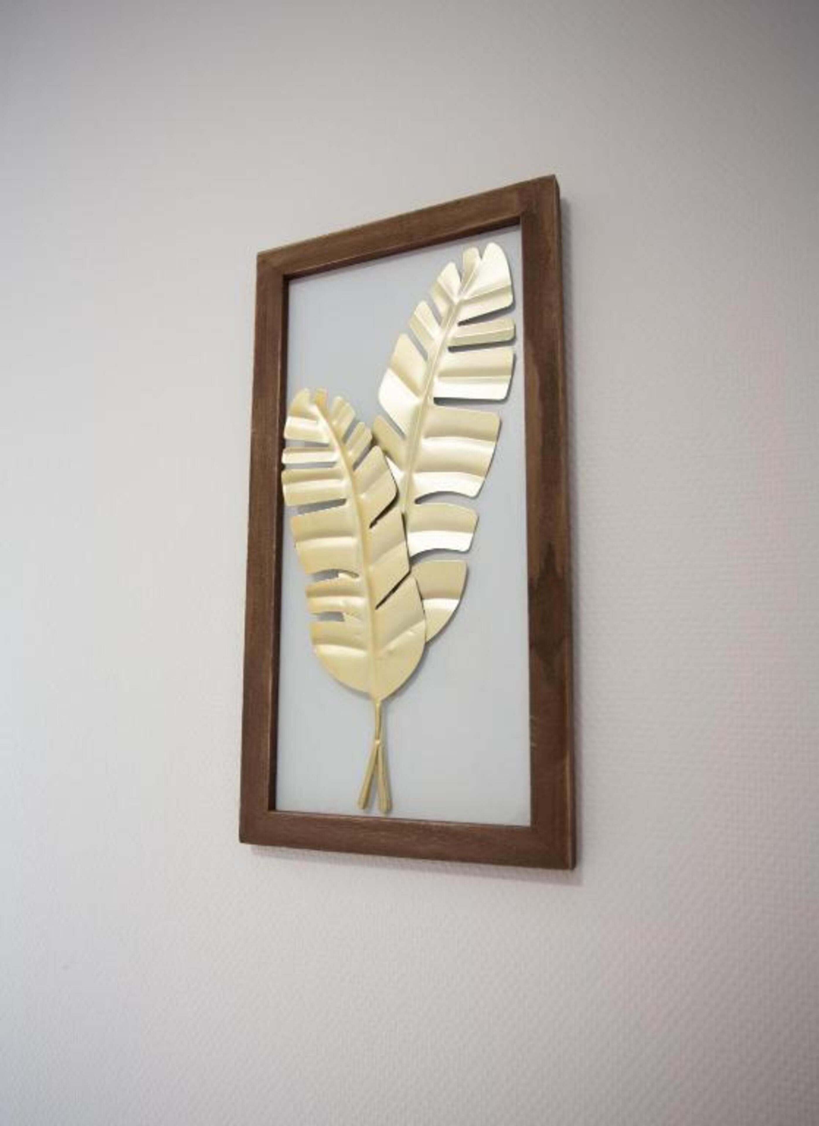 Ein gerahmtes Kunstwerk mit zwei stilisierten Blättern an einer Wand.