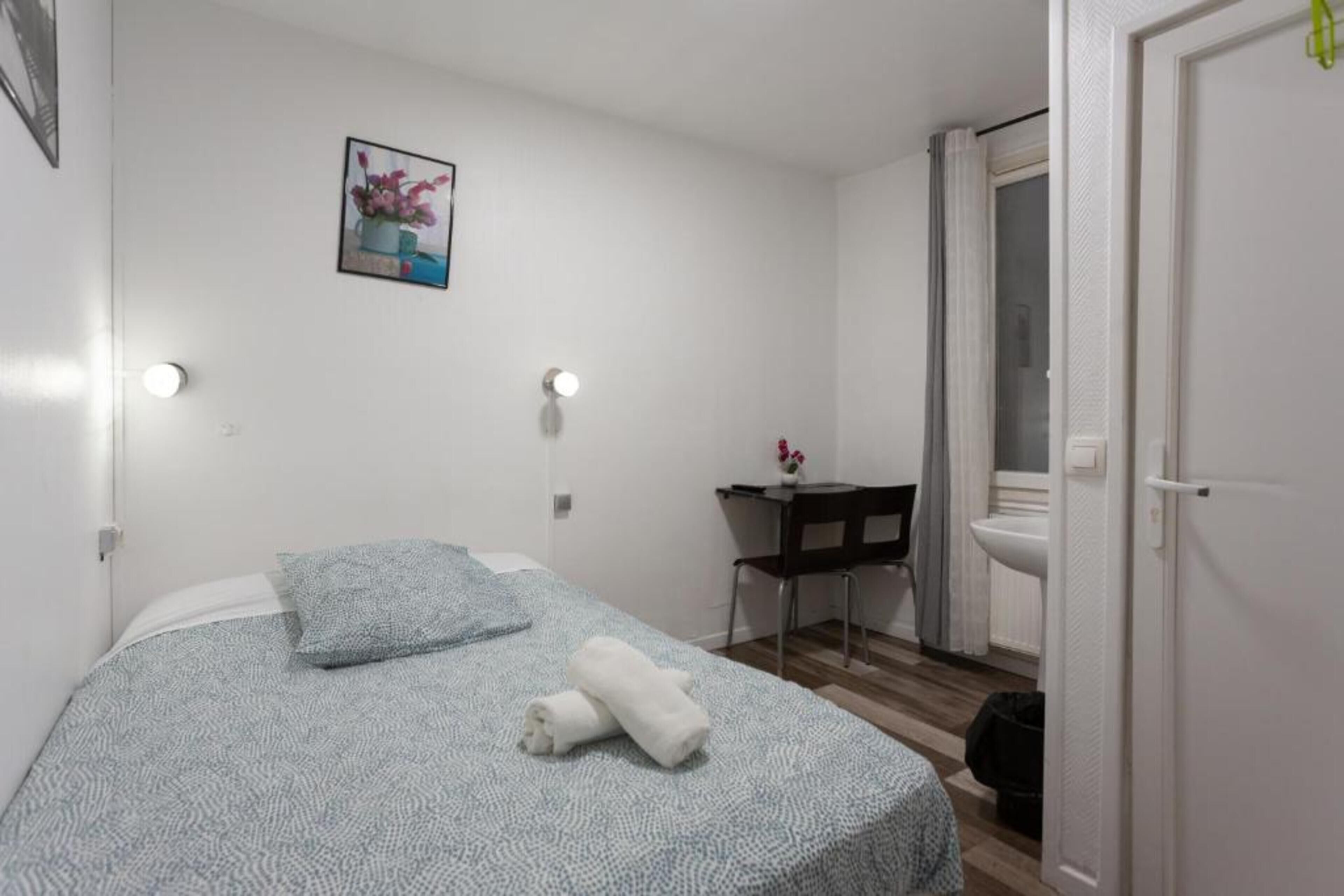 A small, clean room with a bed, a desk, and a toilet.
