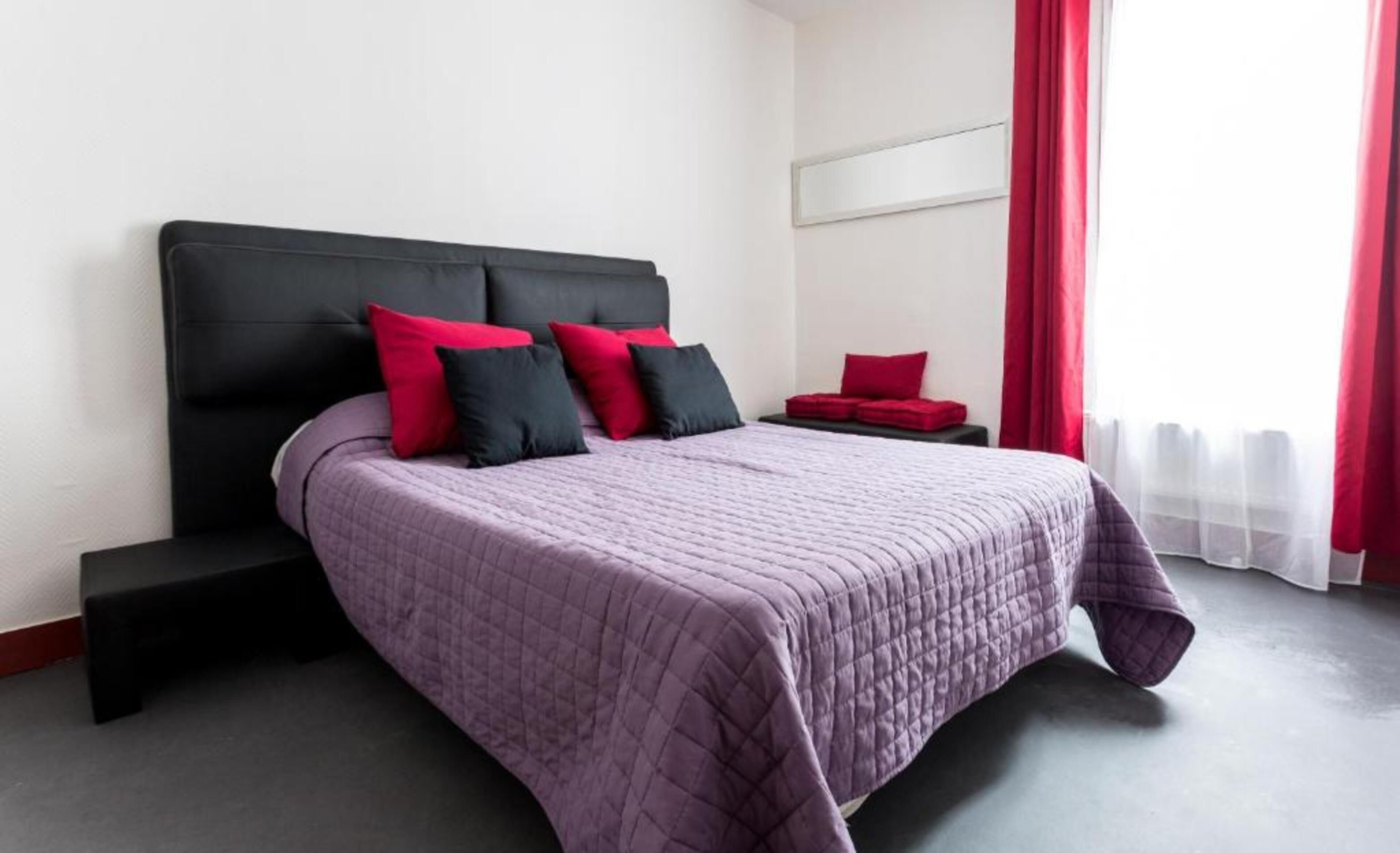 A modern hotel room with a large bed, a black headboard, and red accents.