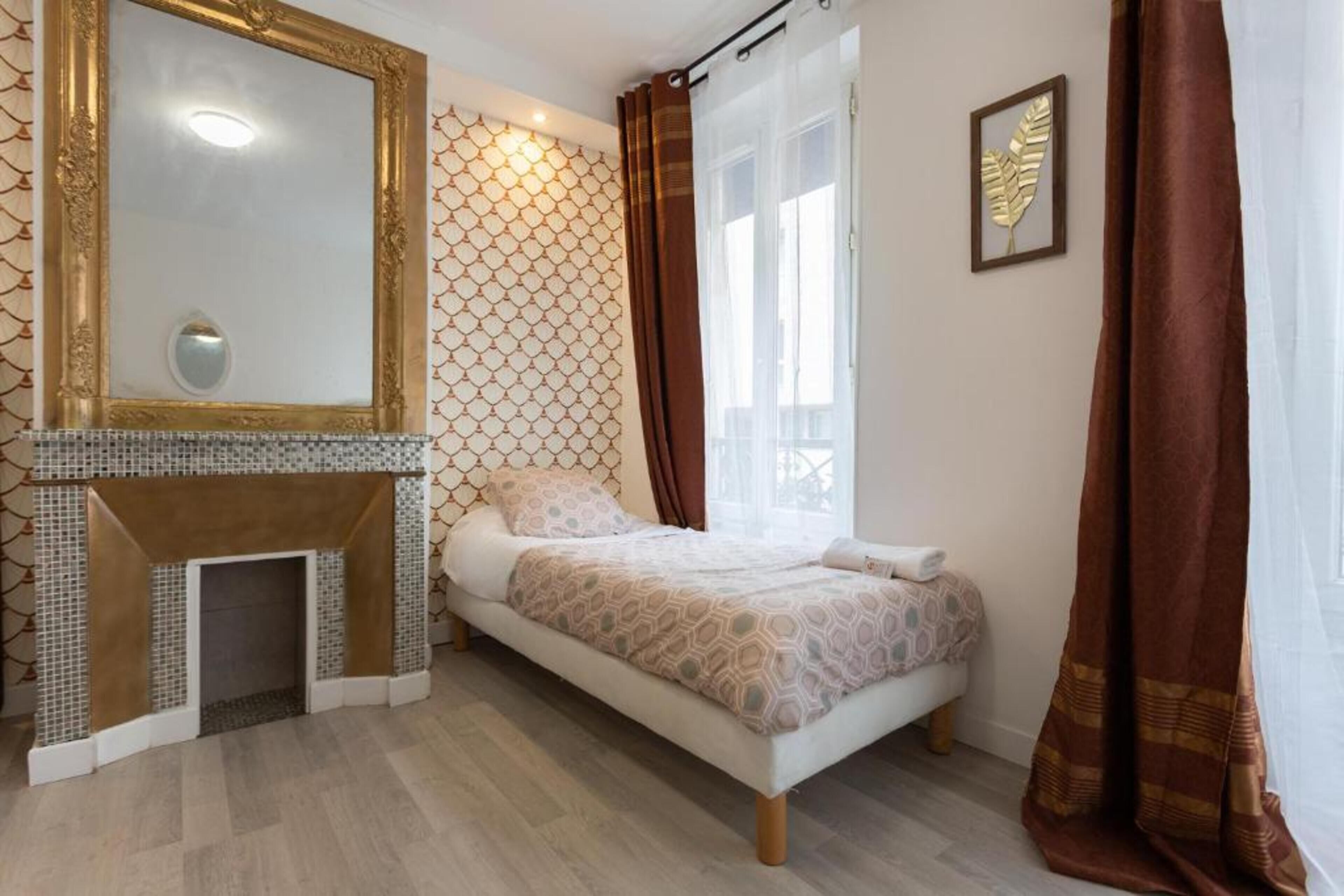 A bedroom with a fireplace, a bed, a large mirror, and a window with curtains.