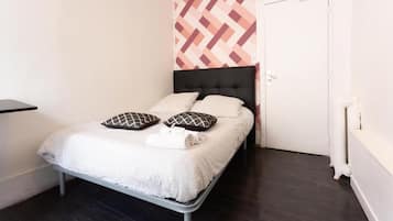 Un lit simple avec une tête de lit à motifs, un mur blanc orné d’un motif géométrique et un radiateur blanc.